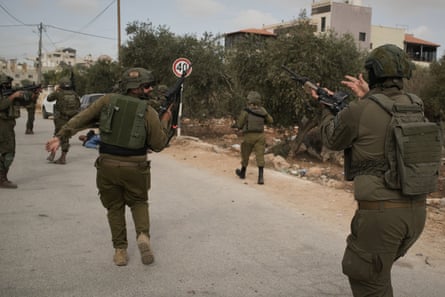 Israeli soldiers moving toward a Palestinian man lying wounded on the road after they shot him during the settler attack.