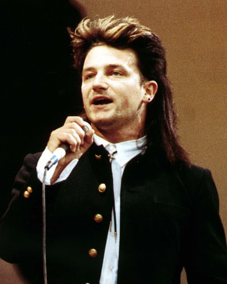 Bono with swept-back shorter hair in front, and the long back hair cascading over his shoulders