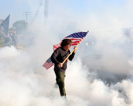 A protester carries a US flag through tear gas launched to clear protesters outside Broadview.