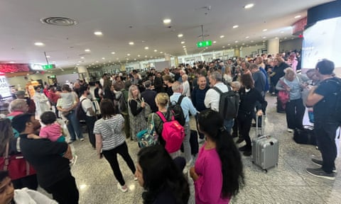 Njerëzit që dëgjojnë një anëtar të stafit të Emirateve (në qendër) ndërsa presin në aeroportin Botëror të Dubait për shkak të përmbytjeve.