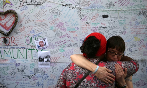 Two women embrace in front of a messages left on a wall of condolence following the blaze at Grenfell Tower. 