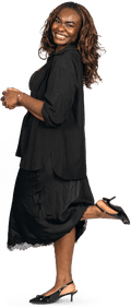 A woman with mid-length reddish-brown hair and wearing a black dress, shirt and heels stands side-on