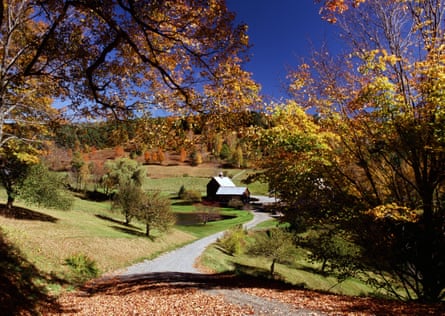 Autumn foliage at Sleepy Hollow Farm against a deep blue sky. A small wooden farmhouse is seen across rolling green fields.