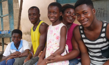 Five African people sitting in a row and smiling, with a girl on the lap of a woman in the middle