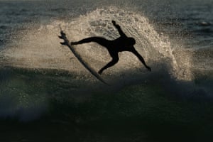 A silhouetted of a person spinning in the air on their surfboard amid the spray at the top a wave