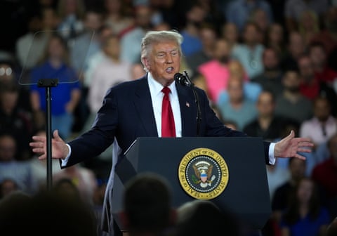 trump speaking at a podium with a crowd out of focus in the foreground and background