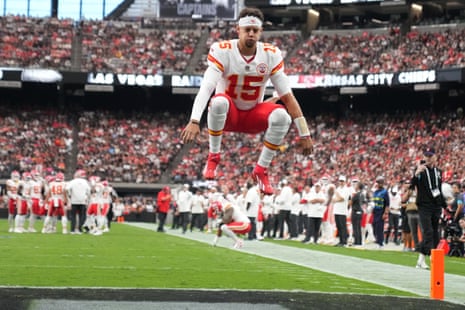 Patrick Mahomes jumps mid-air on the field, knees tucked up, before a game