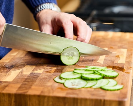 A cucumber being sliced on a wooden board