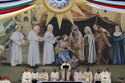  Pope Francis takes mass in Manger Square, Bethlehem, in front of a depiction of the nativity. The mural features the pontiff’s predecessors lined up to pay homage to the infant Jesus who is wrapped in a keffiyeh. 