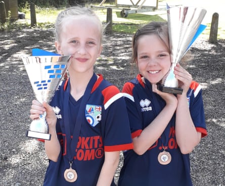 Two young girls in football kit holding trophies