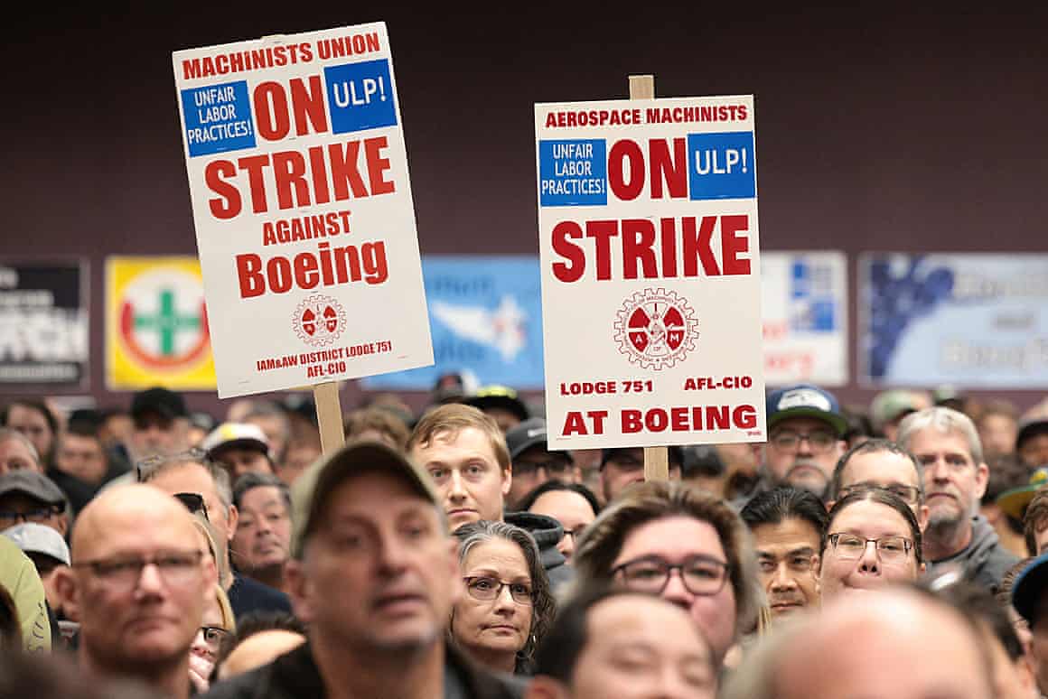 A crowd holding placards reading 'On strike against Boeing', or 'On strike at Boeing'