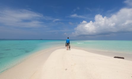 A person standing on the point of a sandbar surrounded by blue water