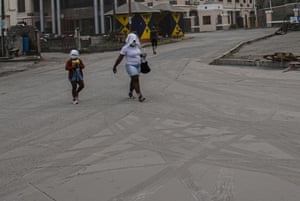 Volcanic ash covers St Vincent – in pictures 11 A woman and a girl walk wearing protective head coverings.
