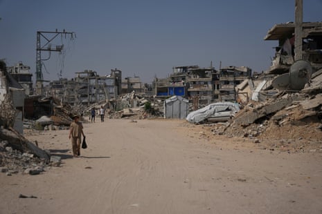 Palestinians walk by the rubble of buildings.