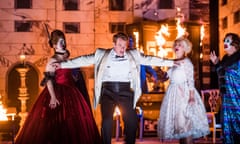 A man in a white tailcoat gestures operatically on a stage with real flames