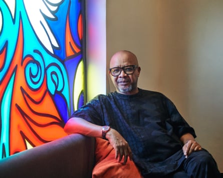 A middle-aged African man sitting on a sofa in front of a stained-glass window