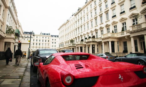 Pedestrians pass a red Ferrari parked outside properties in Kensington, London