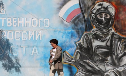 A woman walks past a mural depicting a soldier with the Russian flag
