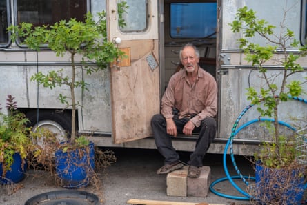 Black sat at entrance of caravan with trees in pots either side