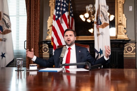 a man in a suit speaks while seated at a table