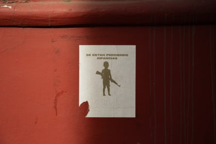 a poster shows a silhouette of a child holding a rifle with the words in Spanish ‘childhoods are being lost’