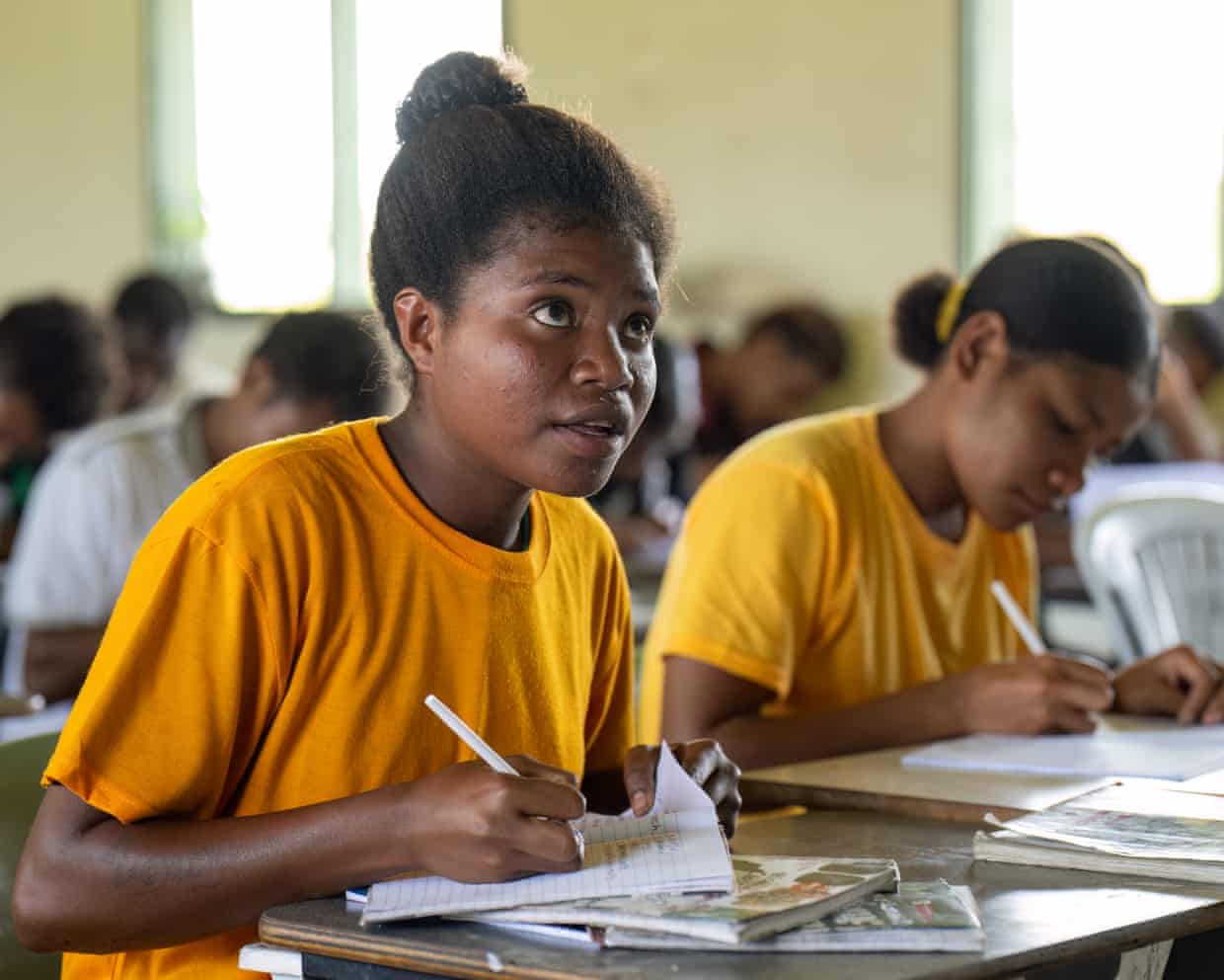Lorna holds a pen in her hand as she sits at a desk in her classroom