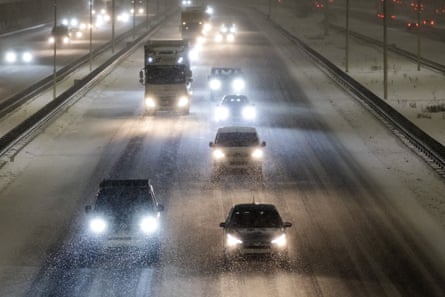 Several lanes of traffic driving in the dark with their lights on, on a snowy motorway
