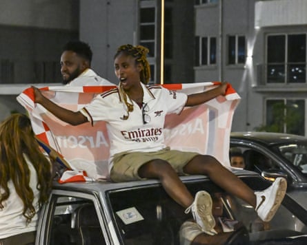 Fans sit in truck and on cab roof wearing Arsenal kit and holding Arsenal flag