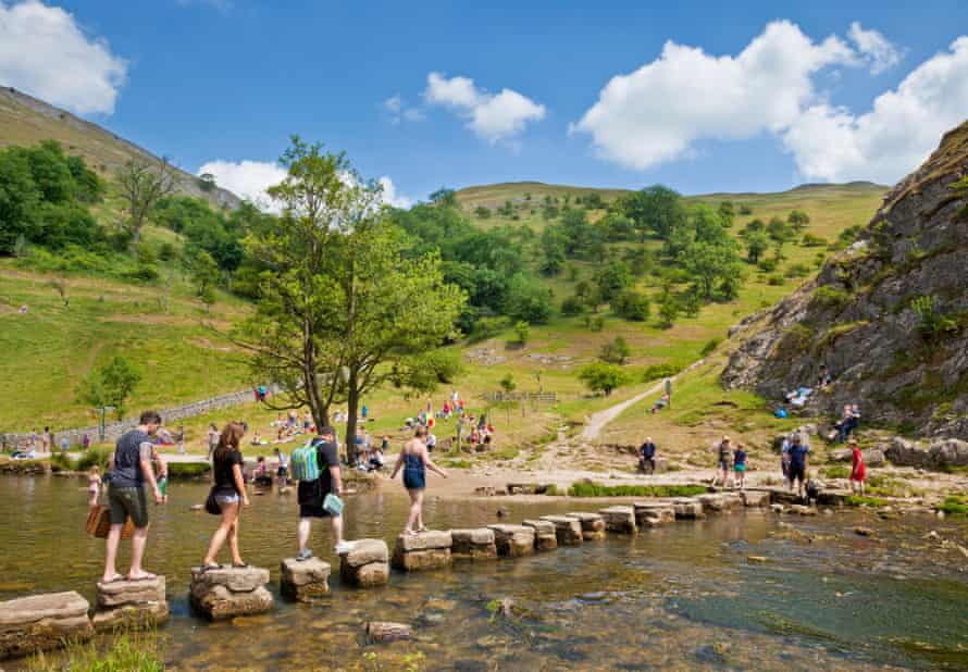 Tourists crossing River Dove on stepping stones in Dovedale Derbyshire peak district national park England