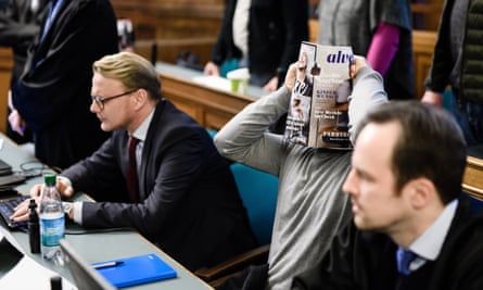 One of the four men on trial holds a magazine in front of his face in the courtroom in Berlin.