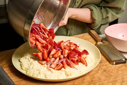 Woman tipping quartered strawberries out of stainless steel bowl on to plate covered in creamt white stracciatella