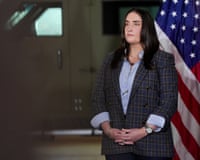 a woman in a suit stands near a US flag