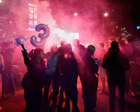 Crowds celebrate election results at night in Belgrade amid red smoke and flares