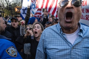 Protesters shout at a demonstration in New York. Some have their fists raise and hold Jewish flags