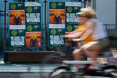 A blurred person cycles past a billboard of posters for Cop28