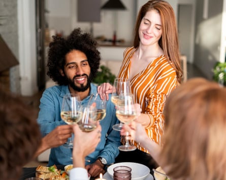 A photograph of young, multi-ethnic friends toasting glasses of white wine over a table.