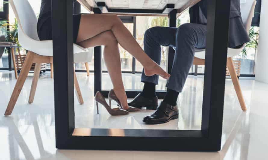 A woman flirtatiously touching leg of man in a suit with her foot under the table.