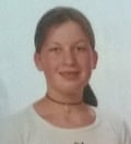 A head and shoulders shot of Daisy Buchanan wearing a white T-shirt and a choker necklace