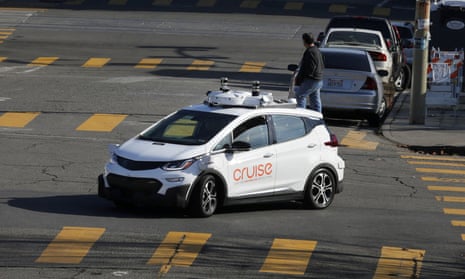 A white car with electronics all over it in the middle of a city intersection.