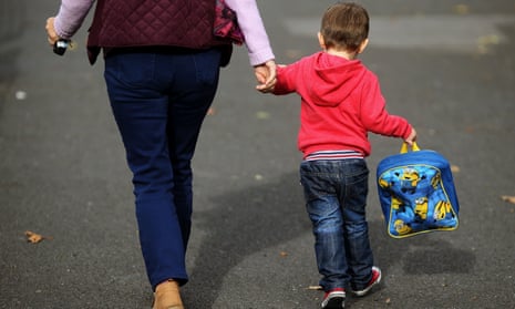 A child carrying a backpack holds a carer's hand.