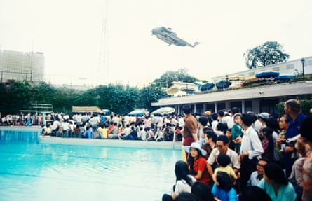 Evacuees inside the US embassy surround the swimming pool as helicopter rescues stranded civilians trying to escape North Vietnamese troops about to capture Saigon.