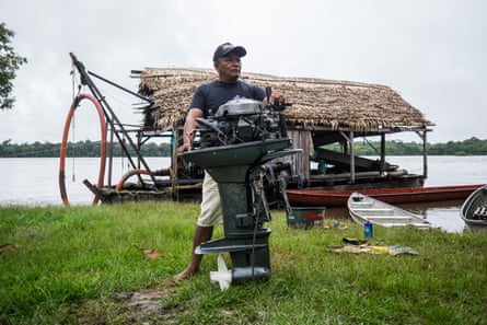 Luis Camelo holding an outboard motor, pictured in front of a mining dredge
