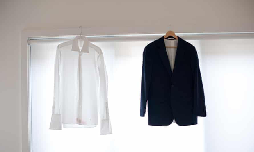 A formal men's shirt and jacket aired on hangers balanced on a window frame.