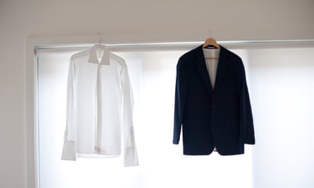 A formal man's shirt and jacket airing on hangers balanced on a window frame.