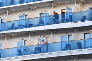 A close-up view of two passengers on their decks onboard the Coral Princess cruise ship. The ship is mostly white but the balconies for each compartment are blue