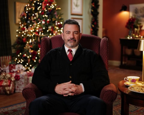 Kimmel sitting with a cup of tea and a plate of biscuits in front of a Christmas tree