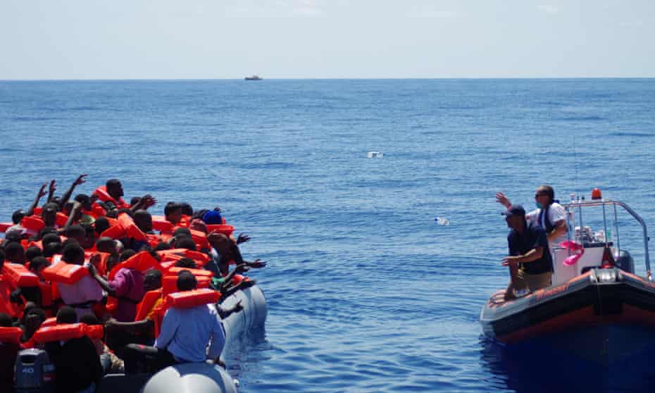 Migrant Offshore Aid Station (MOAS) staff throwing bottles of water from a dinghy to refugees in a rubber raft near Malta. The charity says it has said more than 10,000 lives during its first year in operation.