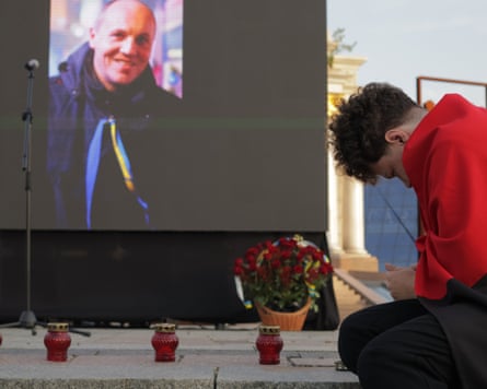 A man wrapped in a red and black flag pays tribute to Andriy Parubiy in front of his picture