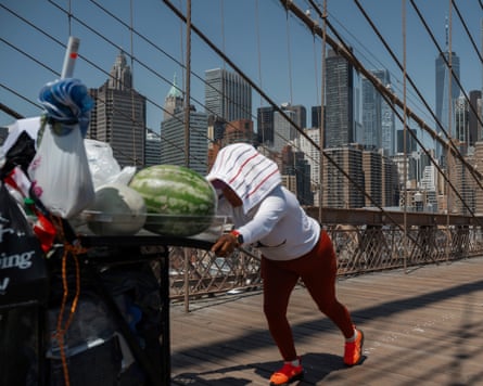 A fruit vendor pushes her cart on the Brooklyn Bridge with cloth over her head