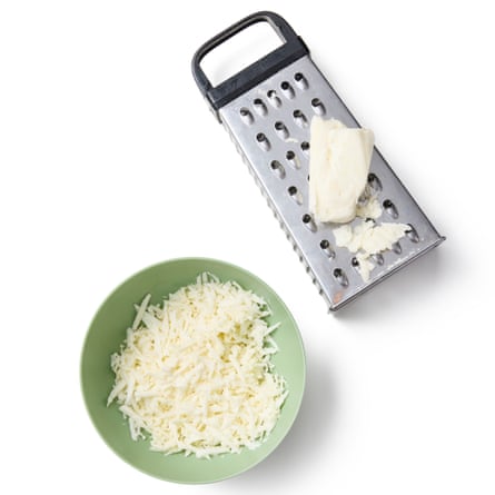 A cheese grater next to grated cheese in a bowl.
